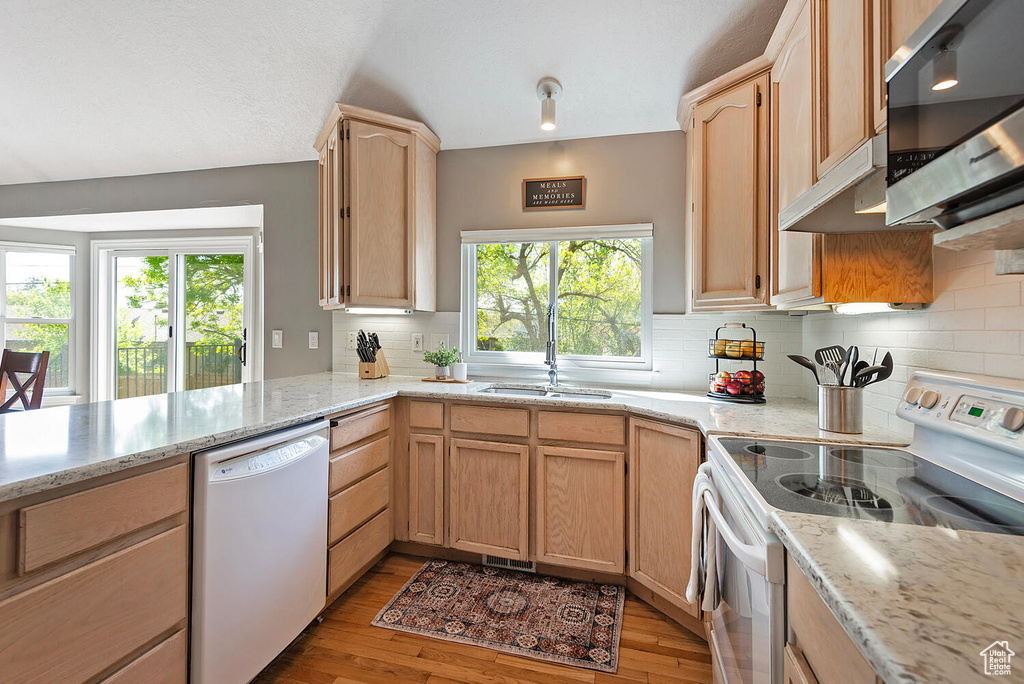 Kitchen with decorative backsplash, light wood-type flooring, a sink, light stone counters, and white appliances