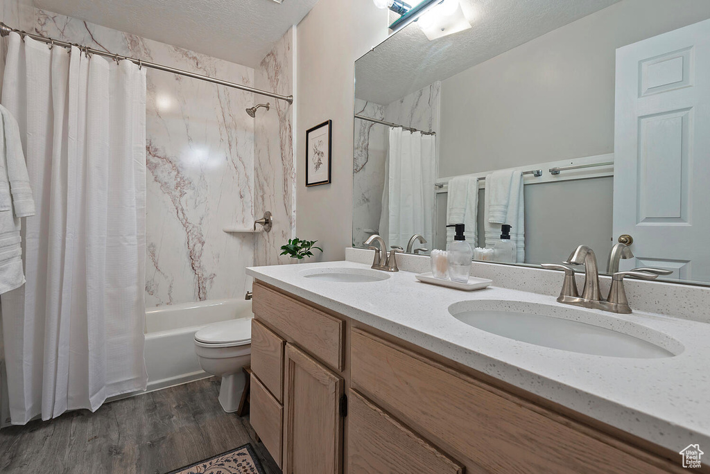 Bathroom with a sink, a textured ceiling, shower / bathtub combination with curtain, and wood finished floors
