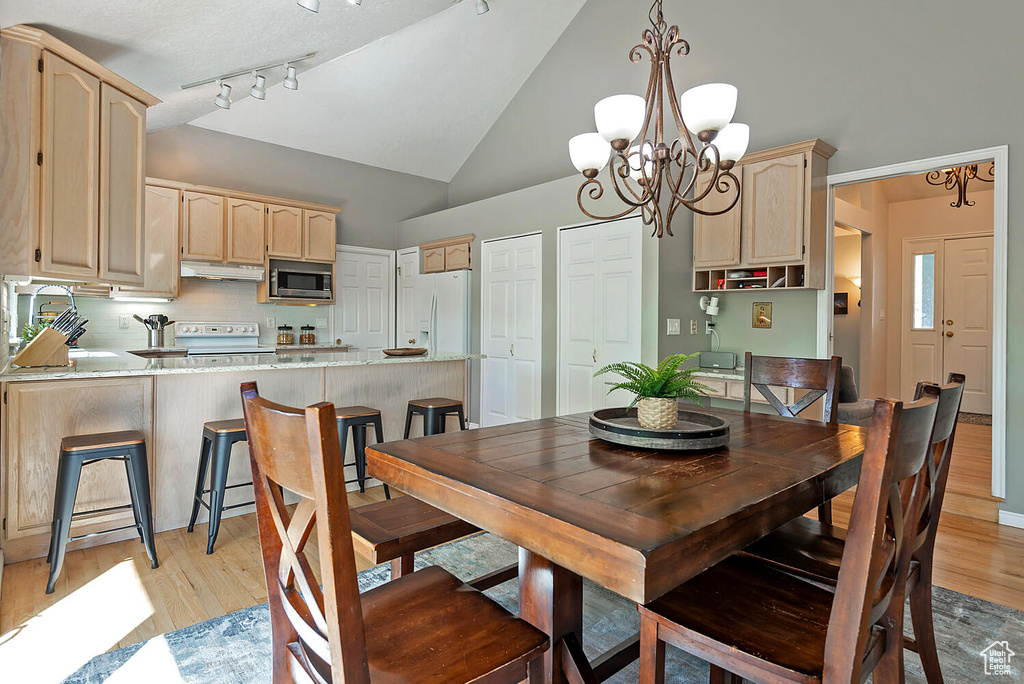 Dining space featuring high vaulted ceiling, a notable chandelier, and light wood-type flooring