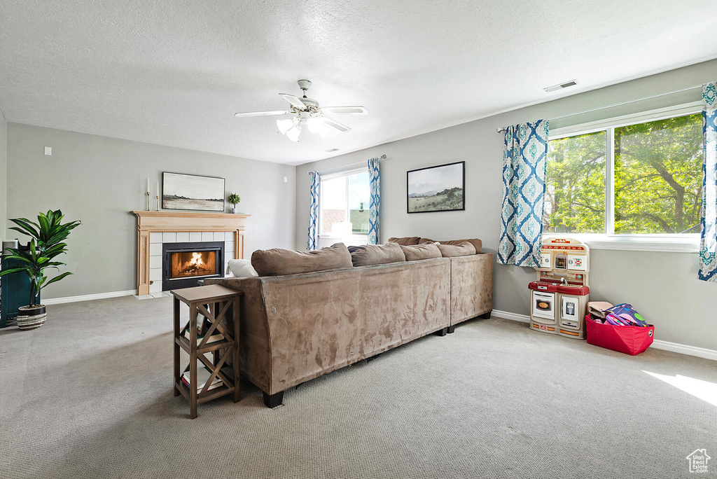 Living room featuring visible vents, carpet floors, baseboards, a tiled fireplace, and a ceiling fan
