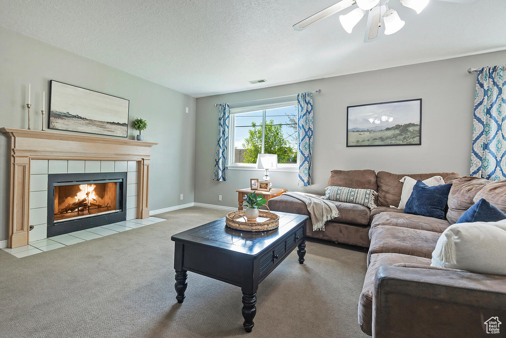 Carpeted living room with ceiling fan, a fireplace, a textured ceiling, baseboards, and visible vents