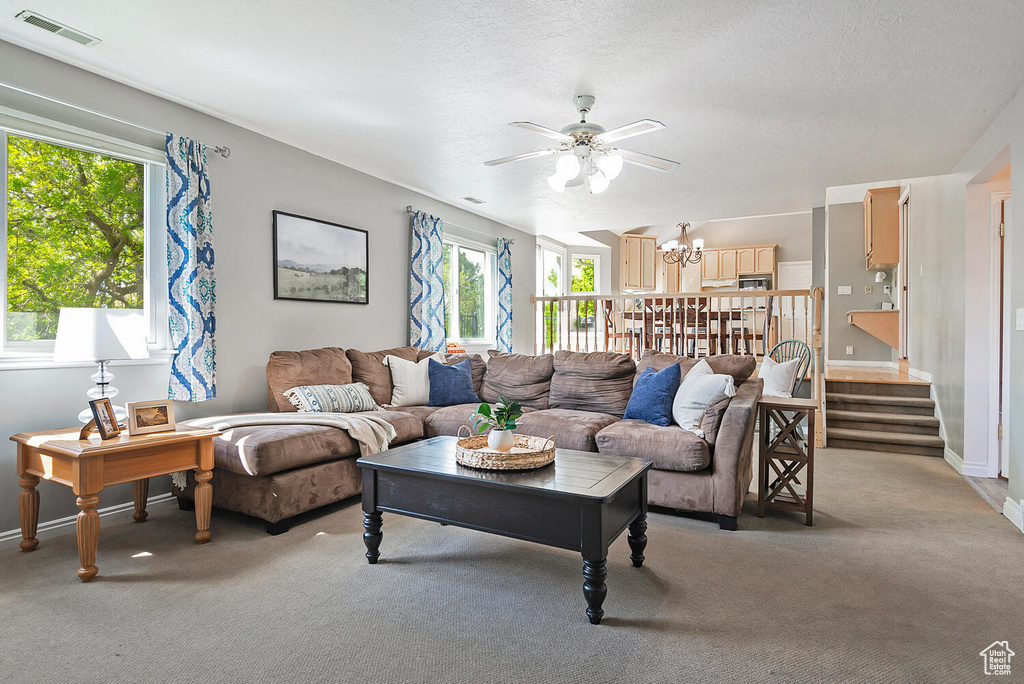 Living area with visible vents, ceiling fan with notable chandelier, a wealth of natural light, and light carpet