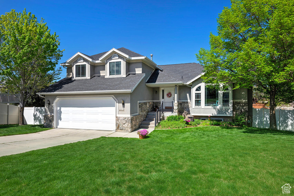 Split level home with a front lawn, fence, stone siding, stucco siding, and driveway
