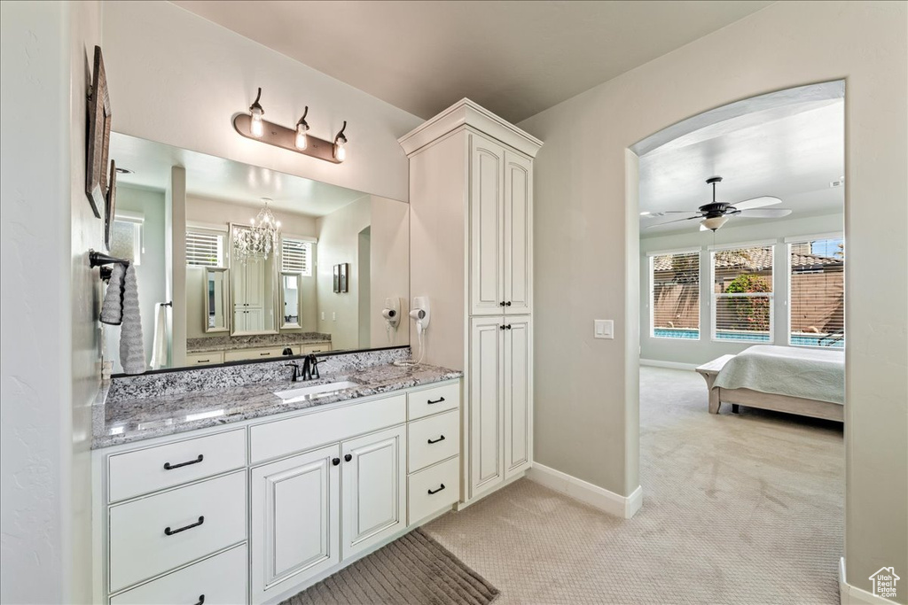 Bathroom featuring baseboards, connected bathroom, ceiling fan with notable chandelier, and vanity