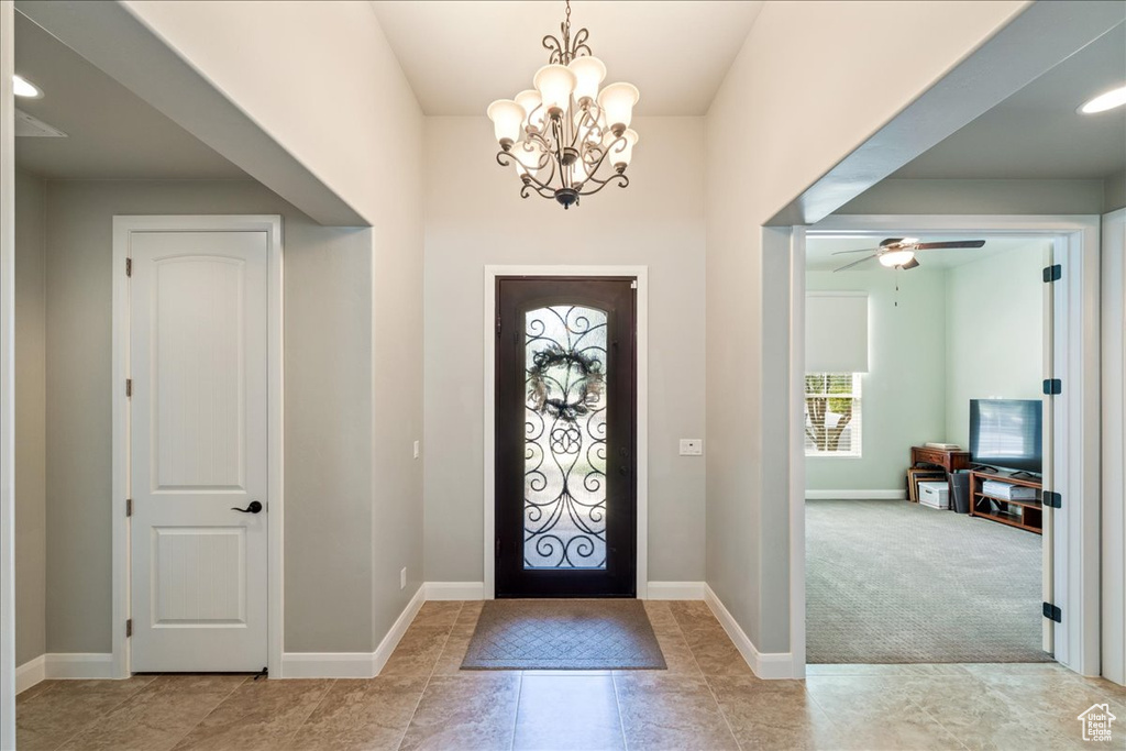 Carpeted entrance foyer with baseboards, ceiling fan with notable chandelier, and tile patterned floors