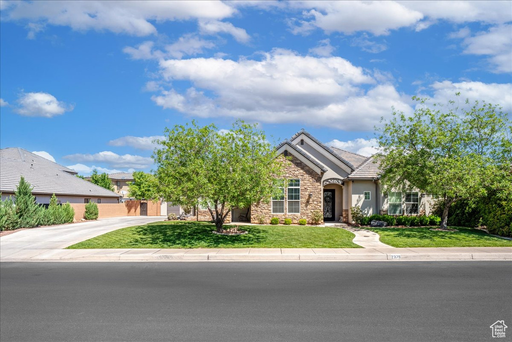 View of front of home with a tiled roof, a front yard, stone siding, and stucco siding