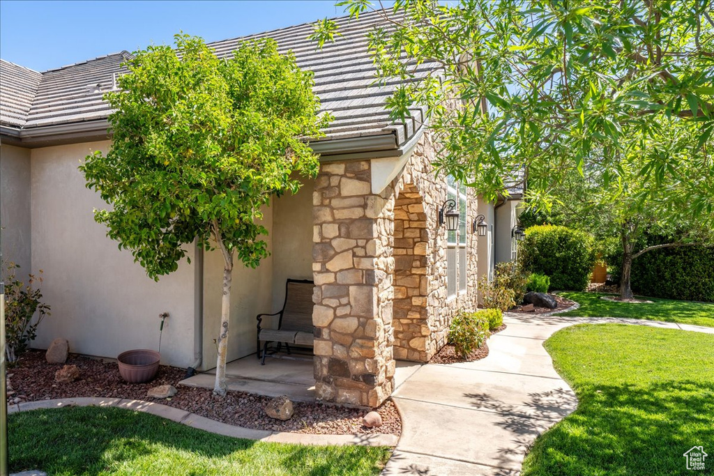 View of side of property featuring a lawn, stucco siding, a tile roof, and stone siding