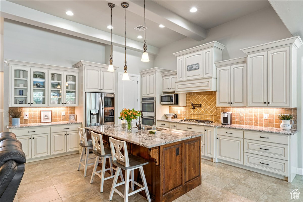 Kitchen with appliances with stainless steel finishes, light stone counters, a breakfast bar area, backsplash, and visible vents