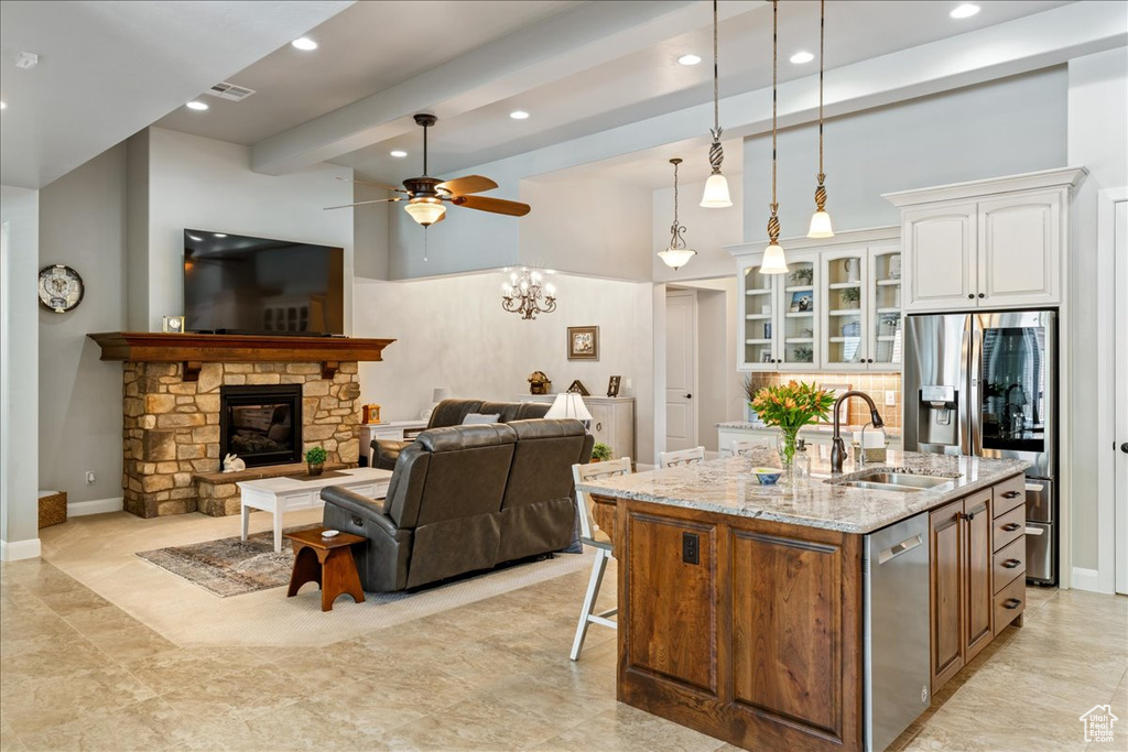Kitchen with ceiling fan, light stone counters, a sink, a kitchen island with sink, and white cabinetry