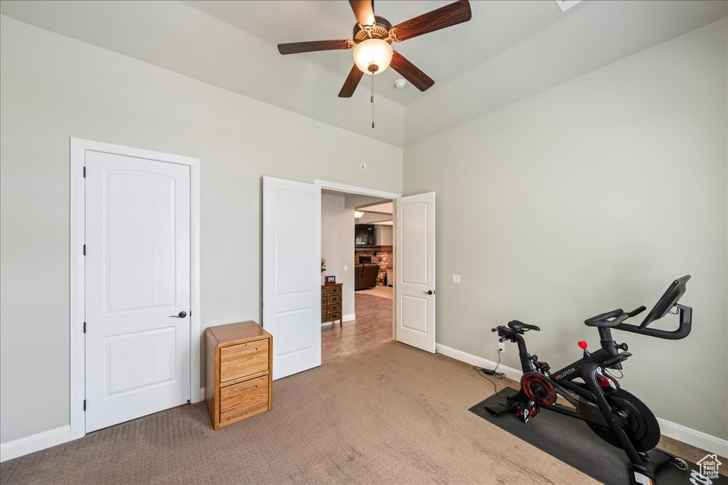 Exercise area with baseboards, ceiling fan, light carpet, and a high ceiling