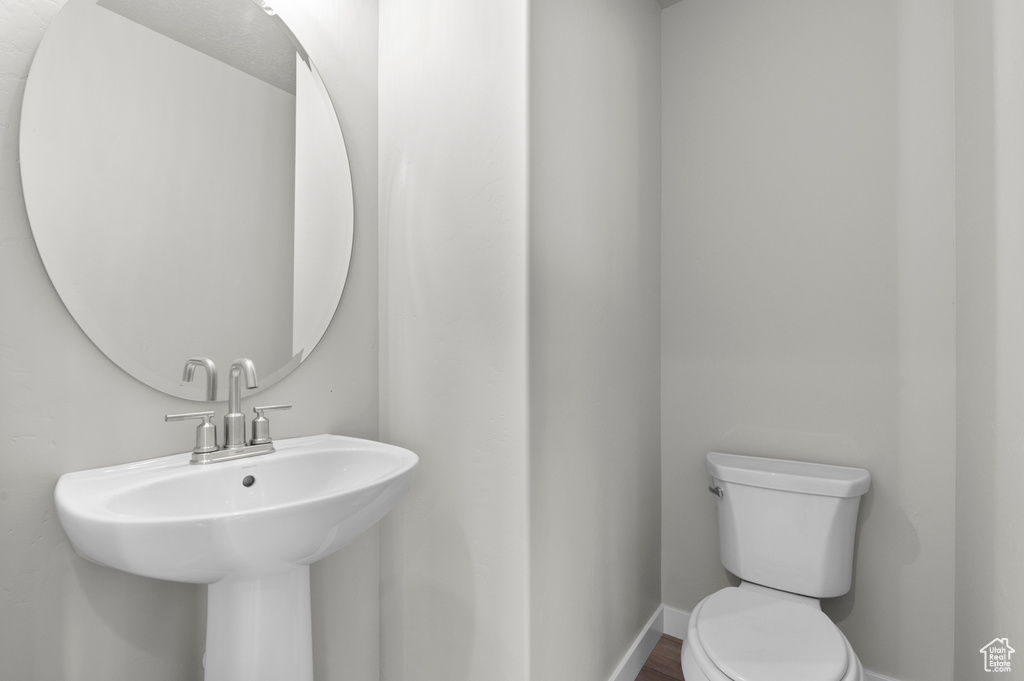 Half bathroom featuring toilet, baseboards, a sink, and wood finished floors
