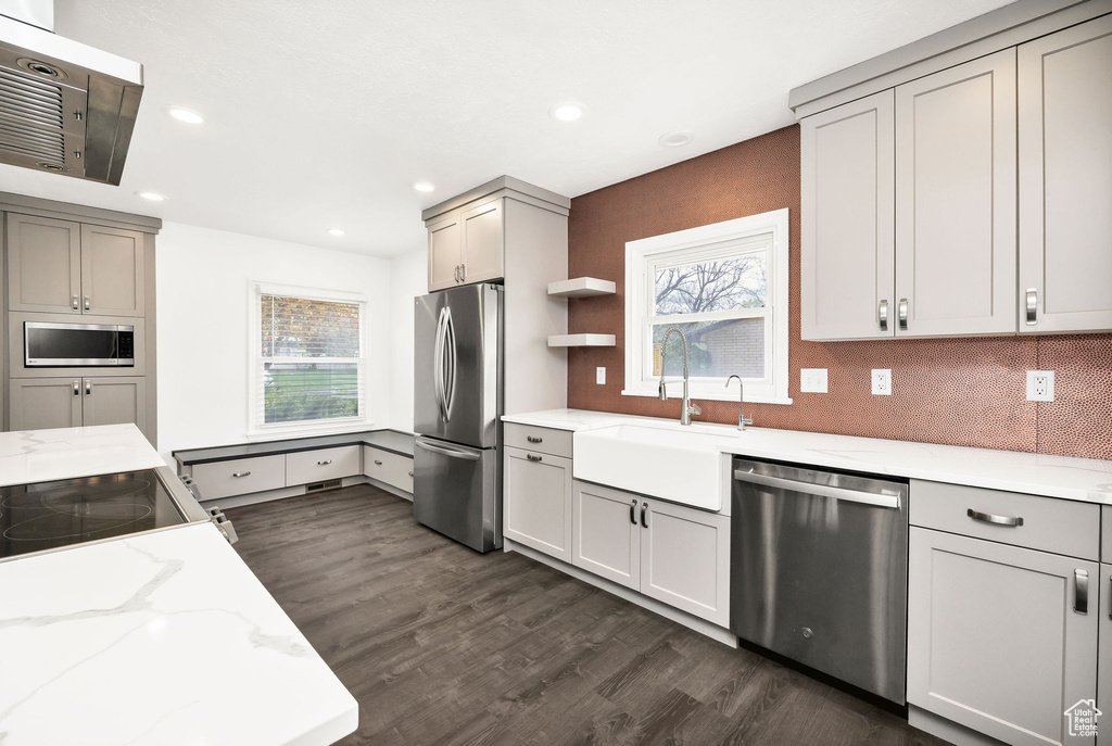 Kitchen featuring decorative backsplash, dark wood-type flooring, light stone counters, a sink, and appliances with stainless steel finishes