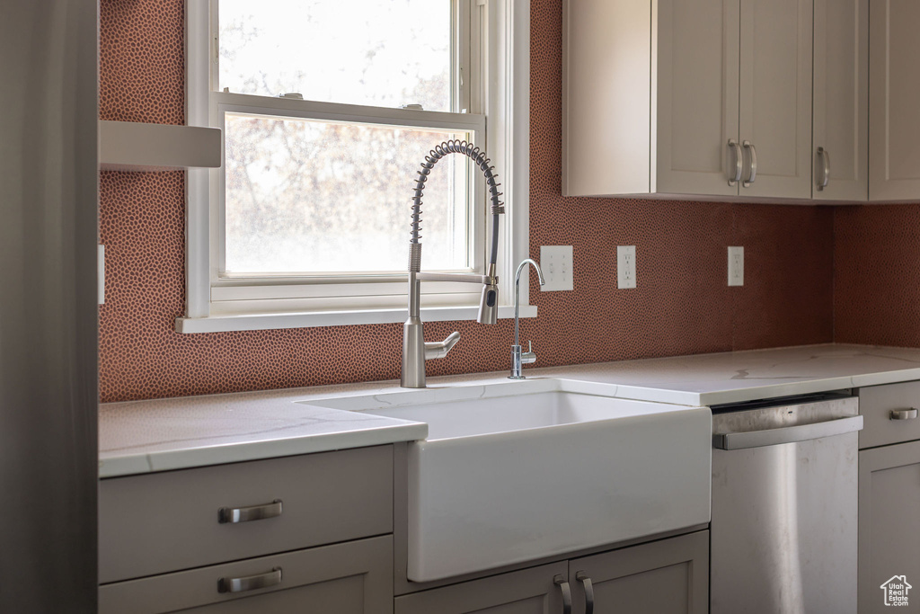 Kitchen featuring a sink, stainless steel dishwasher, gray cabinetry, and light stone countertops