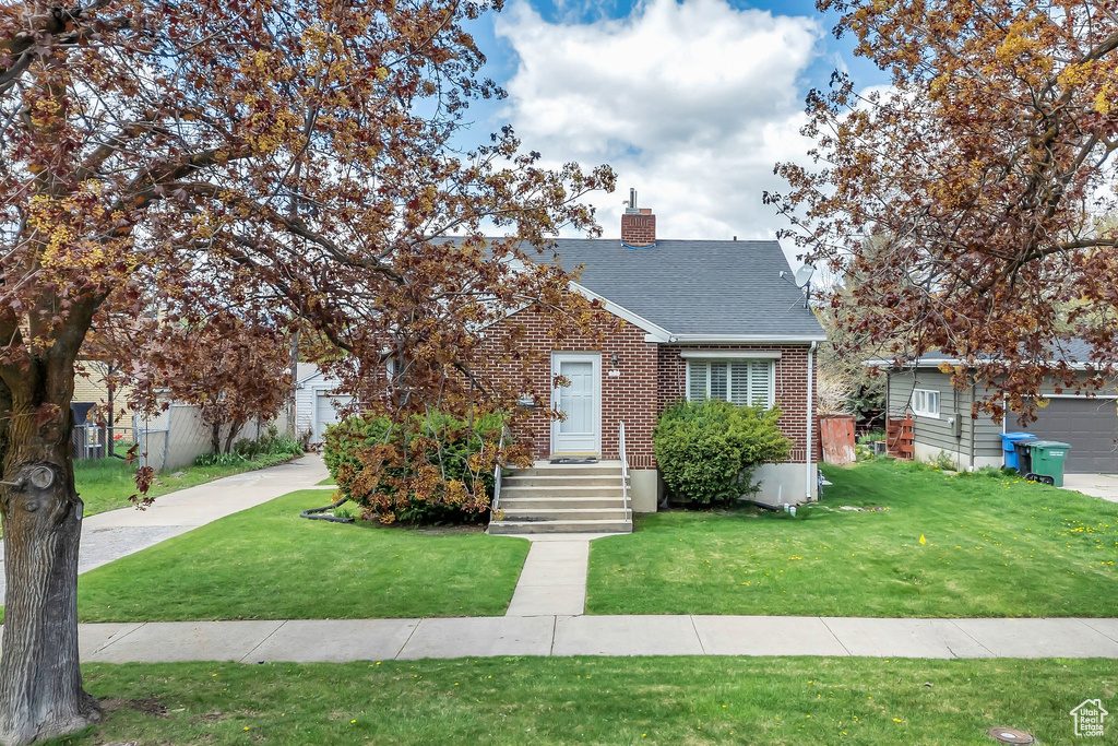 View of front of property featuring a chimney, roof with shingles, brick siding, fence, and a front lawn