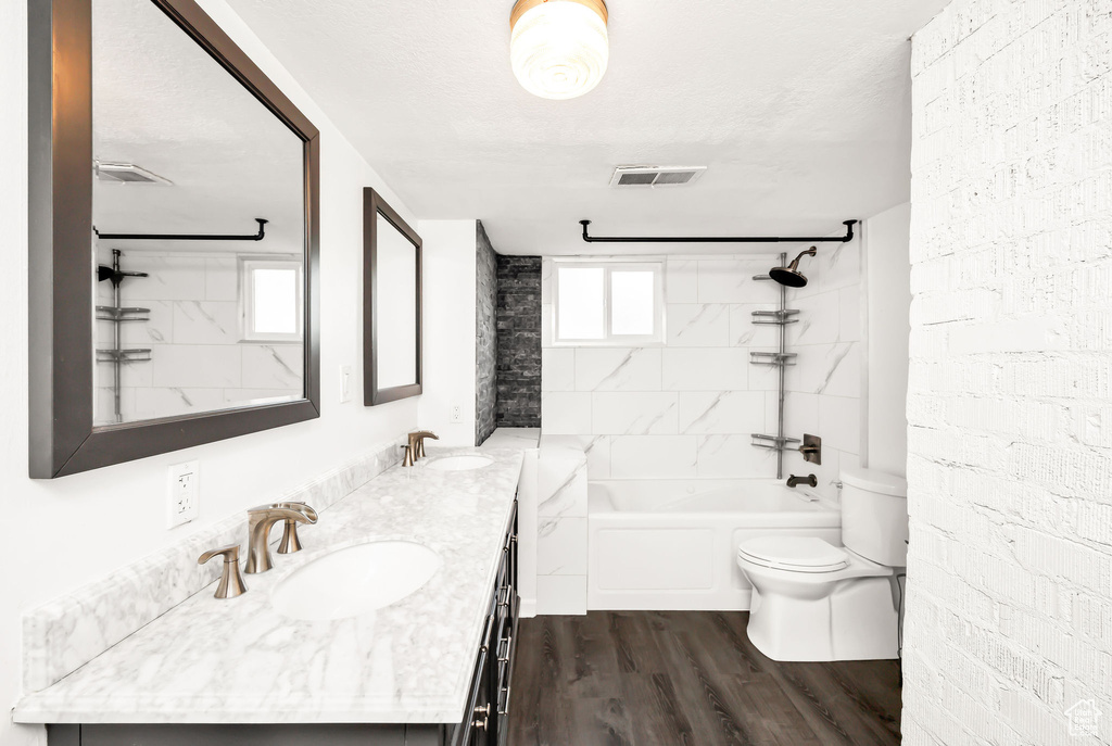 Full bath with a sink, double vanity, toilet, wood finished floors, and visible vents