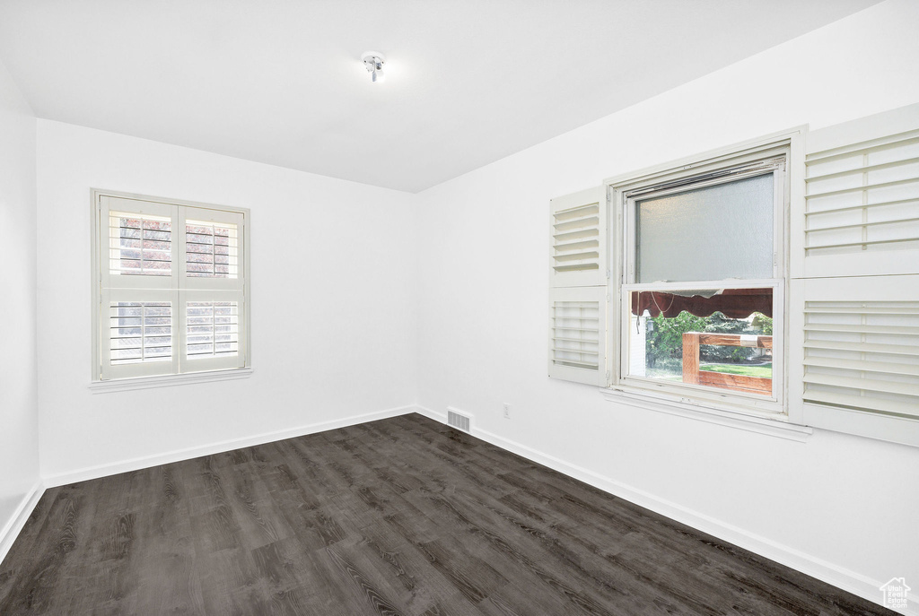 Empty room featuring dark wood-style flooring, baseboards, and a healthy amount of sunlight
