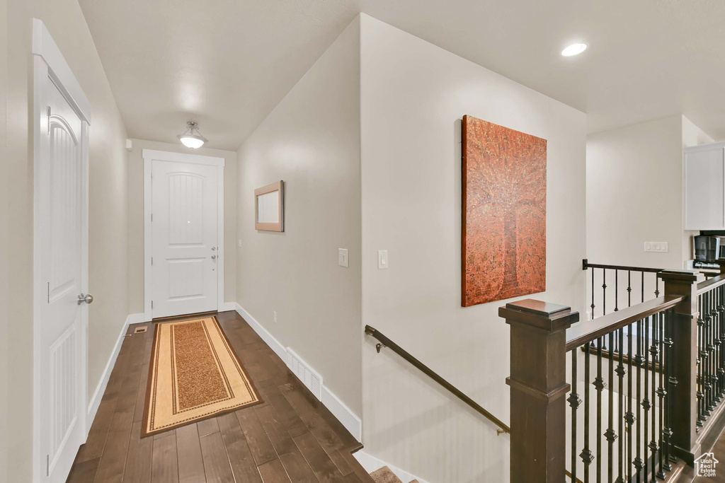 Corridor featuring baseboards, visible vents, dark wood finished floors, and an upstairs landing