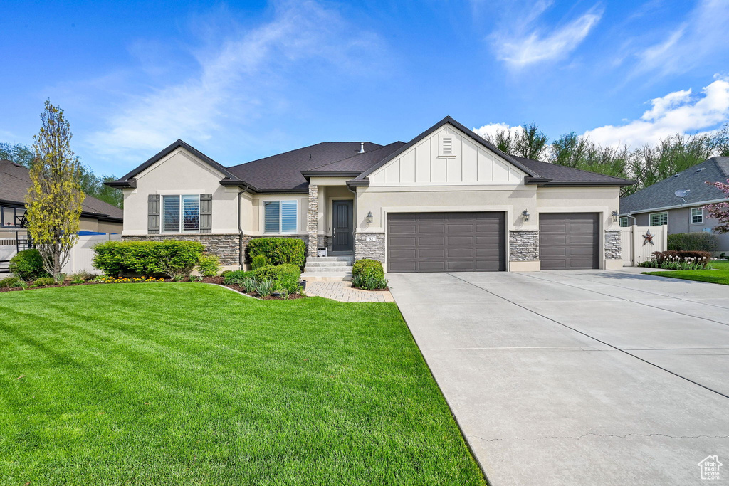 View of front of home with a garage, a front lawn, concrete driveway, stone siding, and stucco siding