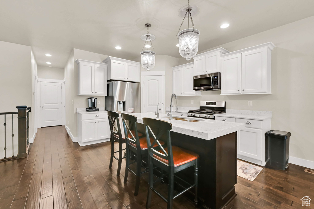 Kitchen with a breakfast bar area, appliances with stainless steel finishes, a sink, baseboards, and dark wood-type flooring