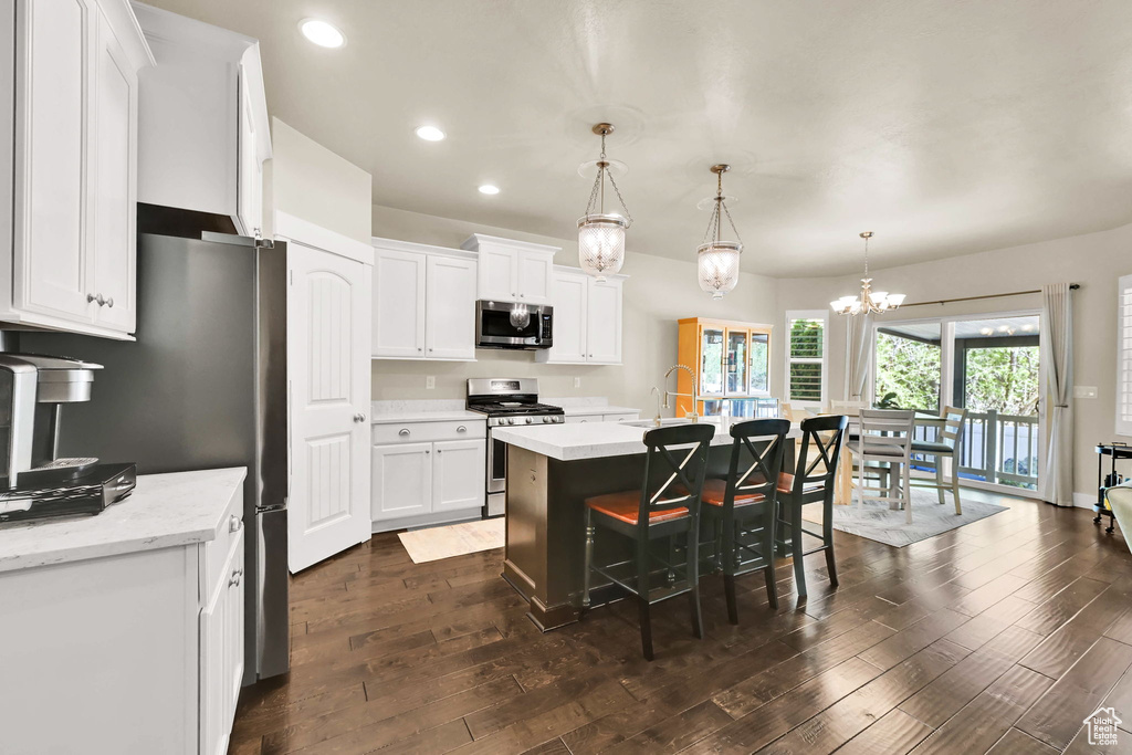Kitchen with a breakfast bar, white cabinets, a sink, dark wood finished floors, and appliances with stainless steel finishes