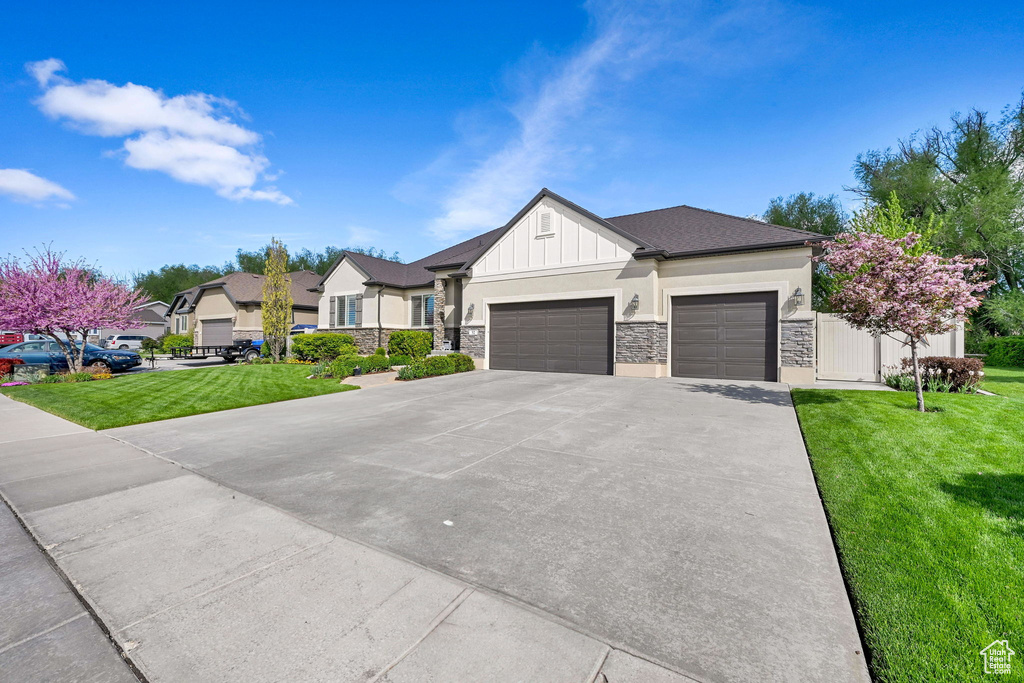 View of front of property with board and batten siding, driveway, a front yard, an attached garage, and stone siding