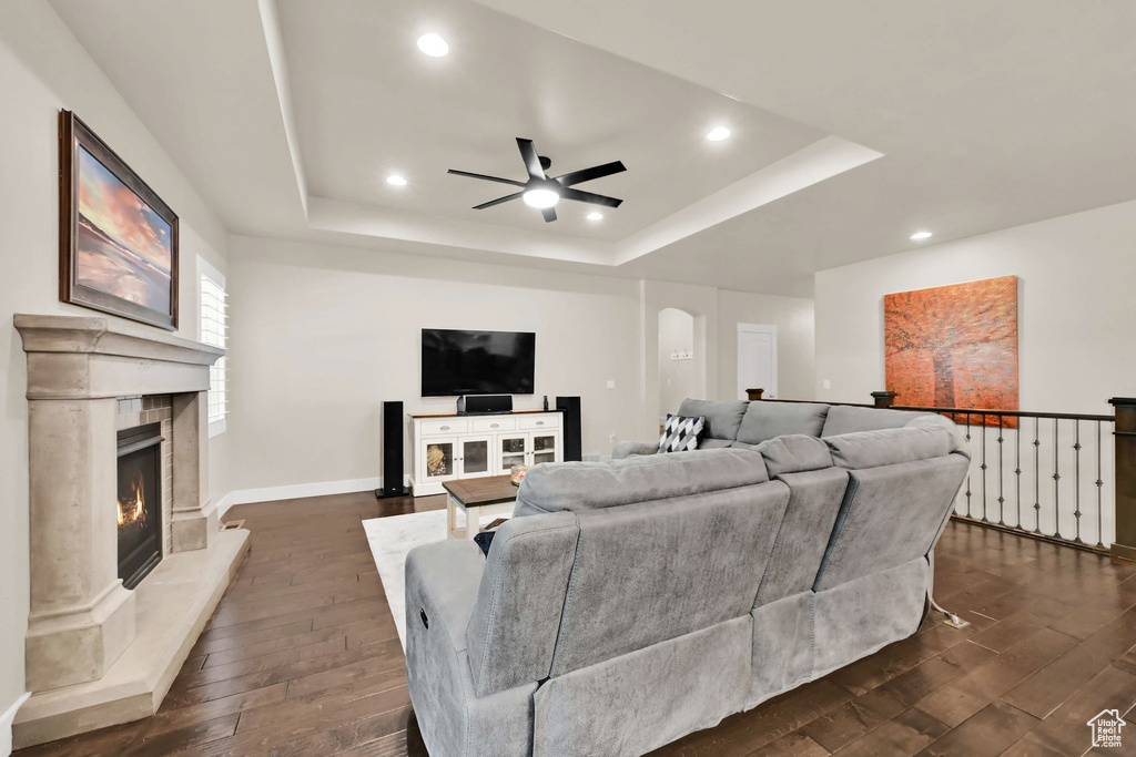 Living room featuring dark wood-type flooring, a ceiling fan, a tray ceiling, and recessed lighting