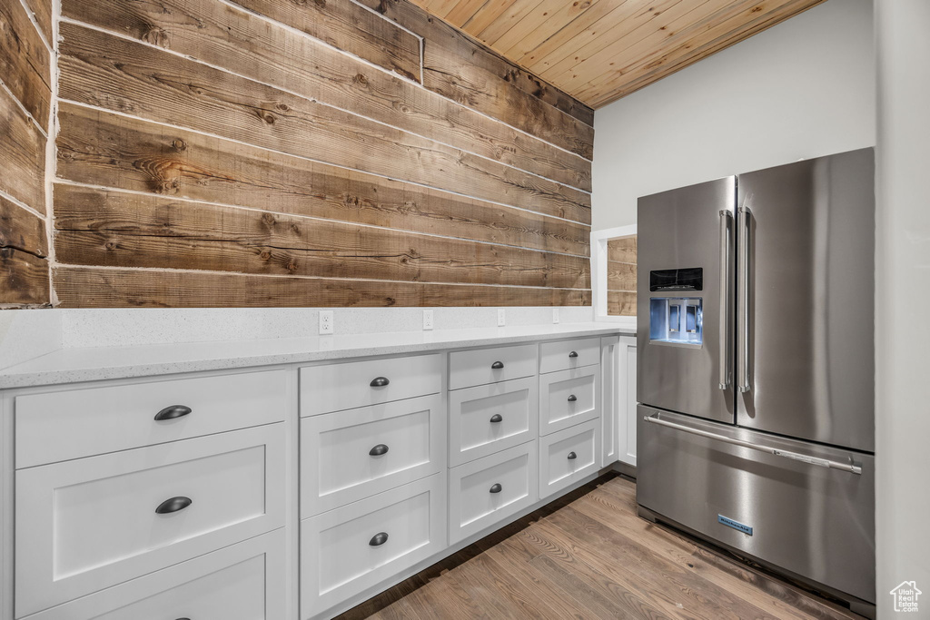 Kitchen featuring wooden walls, light stone countertops, stainless steel fridge, white cabinetry, and wood ceiling