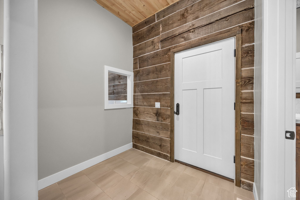Doorway to outside with baseboards, wood walls, wooden ceiling, and vaulted ceiling