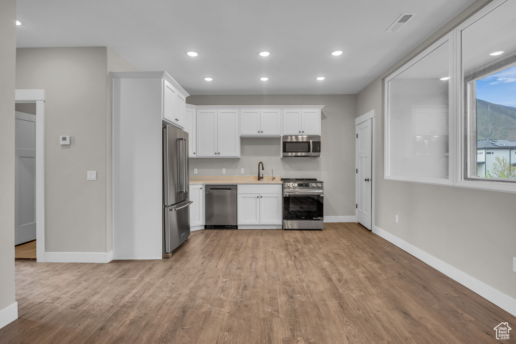 Kitchen with baseboards, light countertops, white cabinetry, light wood-style flooring, and stainless steel appliances