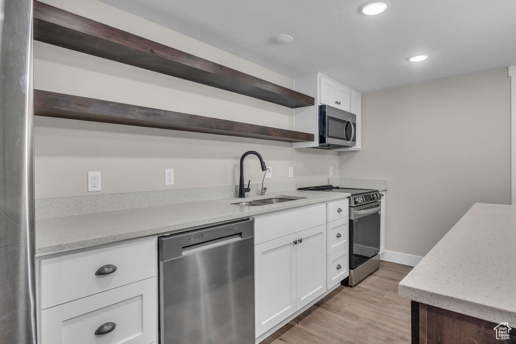 Kitchen featuring open shelves, light wood-type flooring, white cabinetry, a sink, and appliances with stainless steel finishes