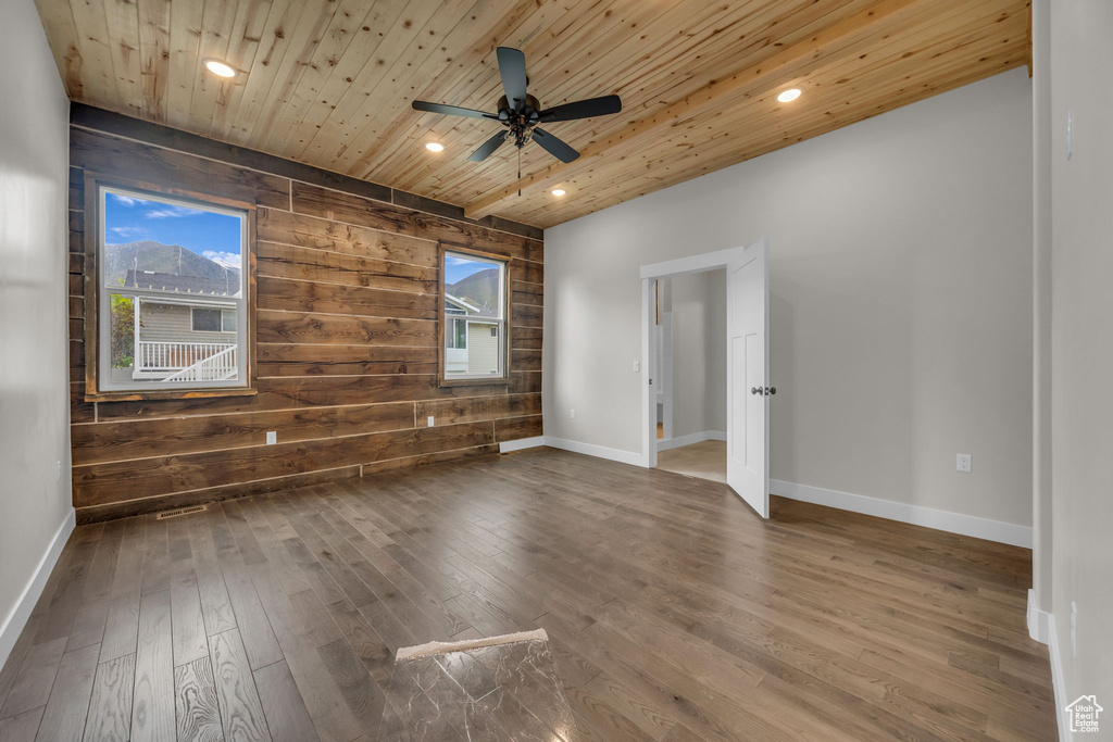 Unfurnished room featuring wood walls, hardwood / wood-style floors, a ceiling fan, baseboards, and wooden ceiling