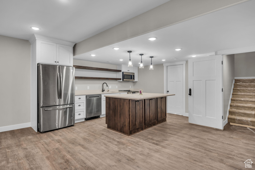 Kitchen with open shelves, light wood-style flooring, appliances with stainless steel finishes, and light countertops