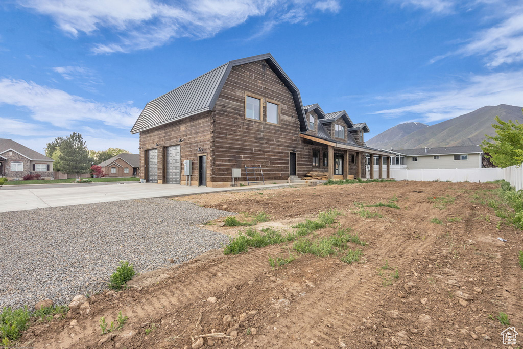 View of side of property with metal roof, fence, a gambrel roof, concrete driveway, and an attached garage
