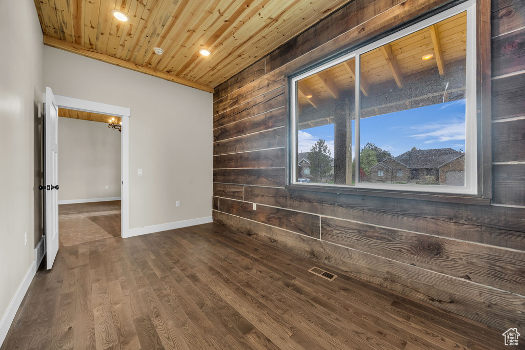 Empty room featuring wood ceiling, visible vents, wood walls, baseboards, and dark wood-type flooring