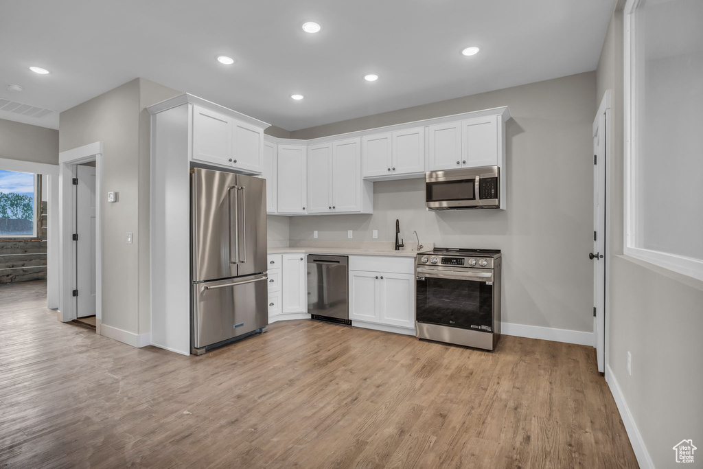 Kitchen featuring appliances with stainless steel finishes, baseboards, light wood-style flooring, and white cabinetry