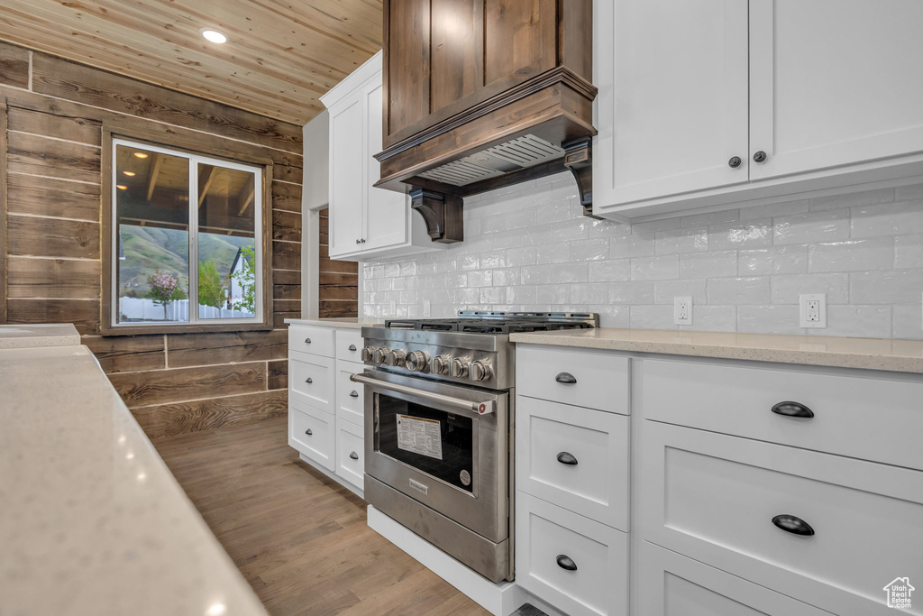 Kitchen featuring wood finished floors, high end stainless steel range, white cabinets, wooden ceiling, and backsplash