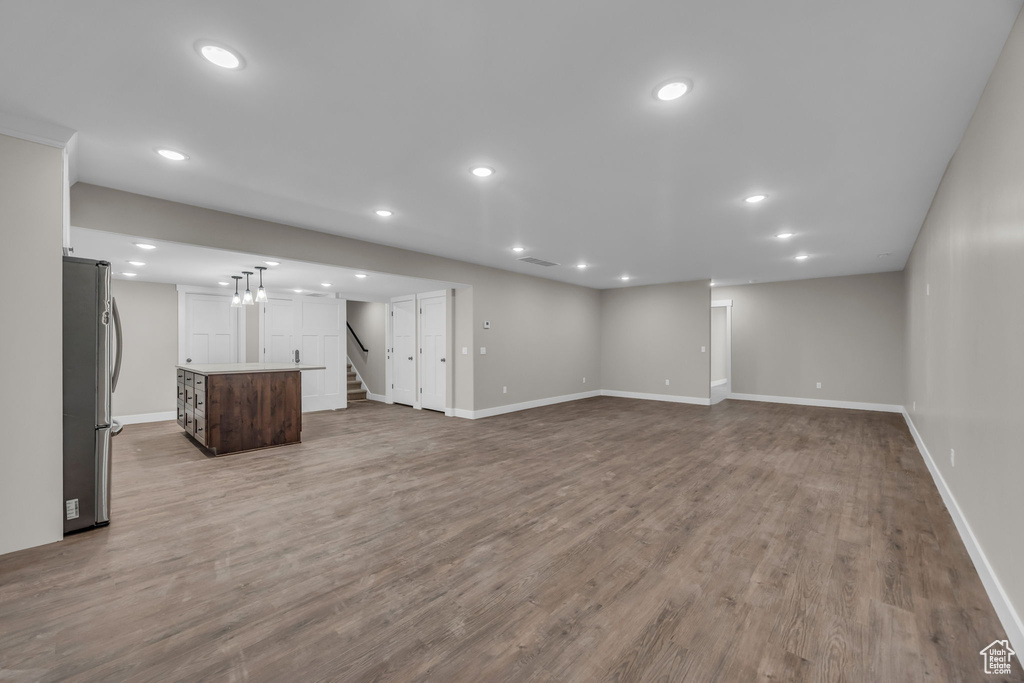 Unfurnished living room featuring recessed lighting, baseboards, wood finished floors, and stairway