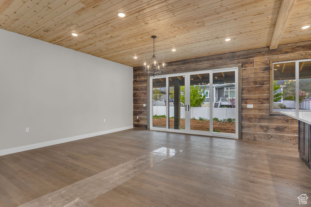 Unfurnished dining area with wood walls, an inviting chandelier, wooden ceiling, and a wealth of natural light