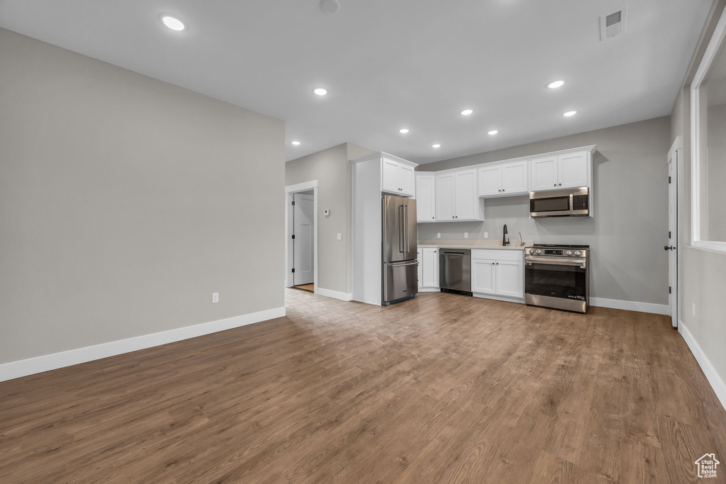 Kitchen with wood finished floors, baseboards, white cabinetry, a sink, and stainless steel appliances