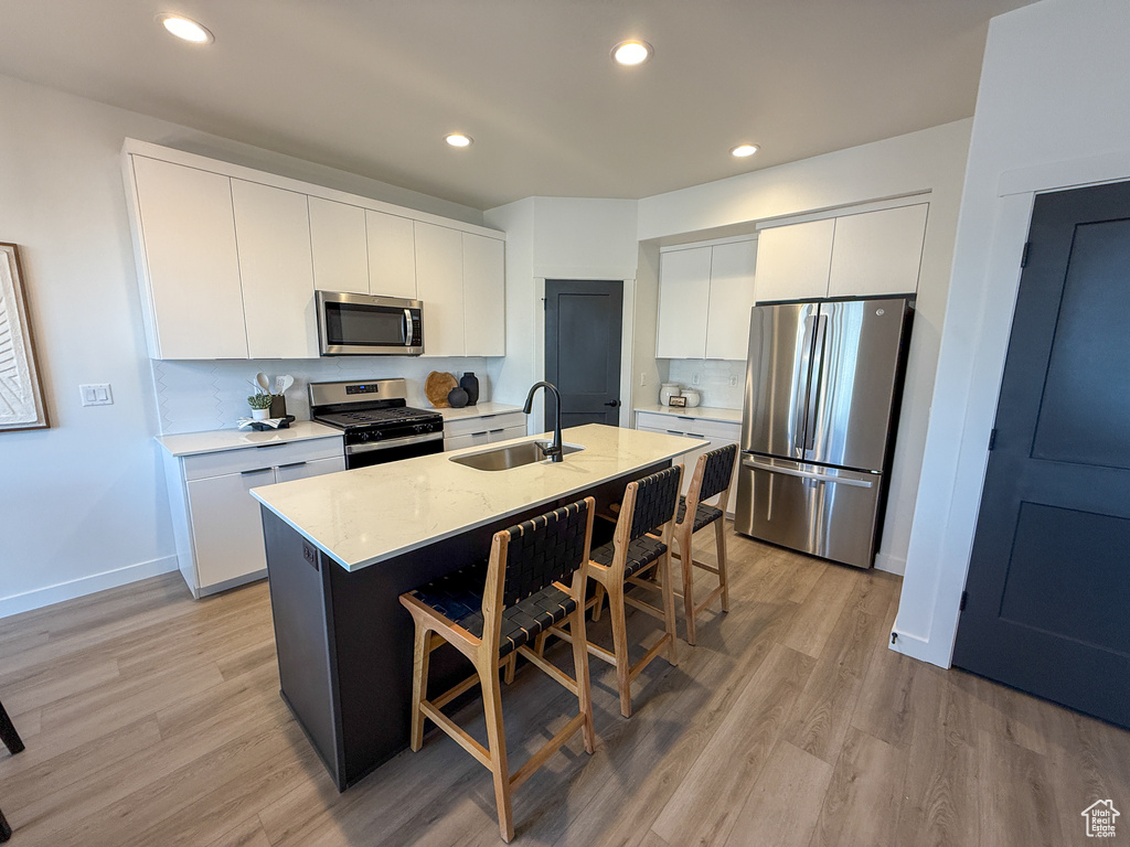 Kitchen featuring appliances with stainless steel finishes, a sink, light wood-style flooring, and a kitchen bar