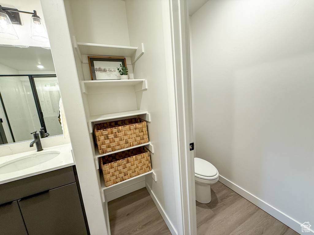Full bath featuring vanity, toilet, baseboards, wood finished floors, and a shower with door