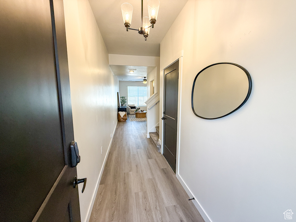 Hall featuring baseboards, light wood-style flooring, and a notable chandelier