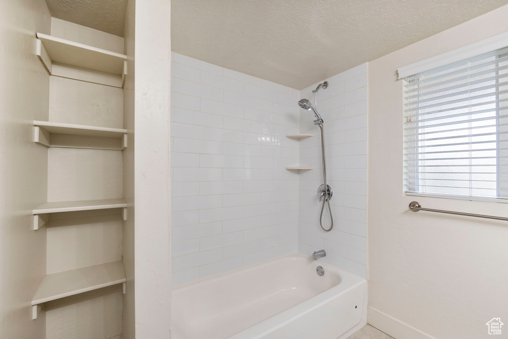 Bathroom featuring a textured ceiling, baseboards, and washtub / shower combination