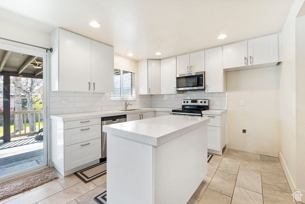 Kitchen featuring decorative backsplash, a kitchen island, white cabinetry, a sink, and appliances with stainless steel finishes
