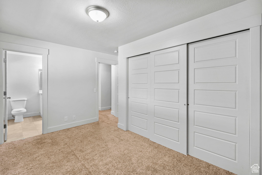 Unfurnished bedroom with a closet, baseboards, ensuite bathroom, and light carpet