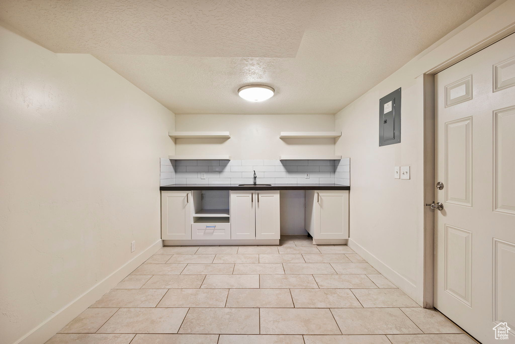 Kitchen with open shelves, a sink, dark countertops, a textured ceiling, and decorative backsplash