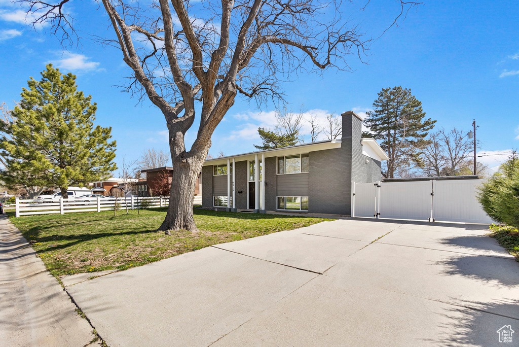 View of front facade featuring a front yard, a chimney, fence, brick siding, and a gate