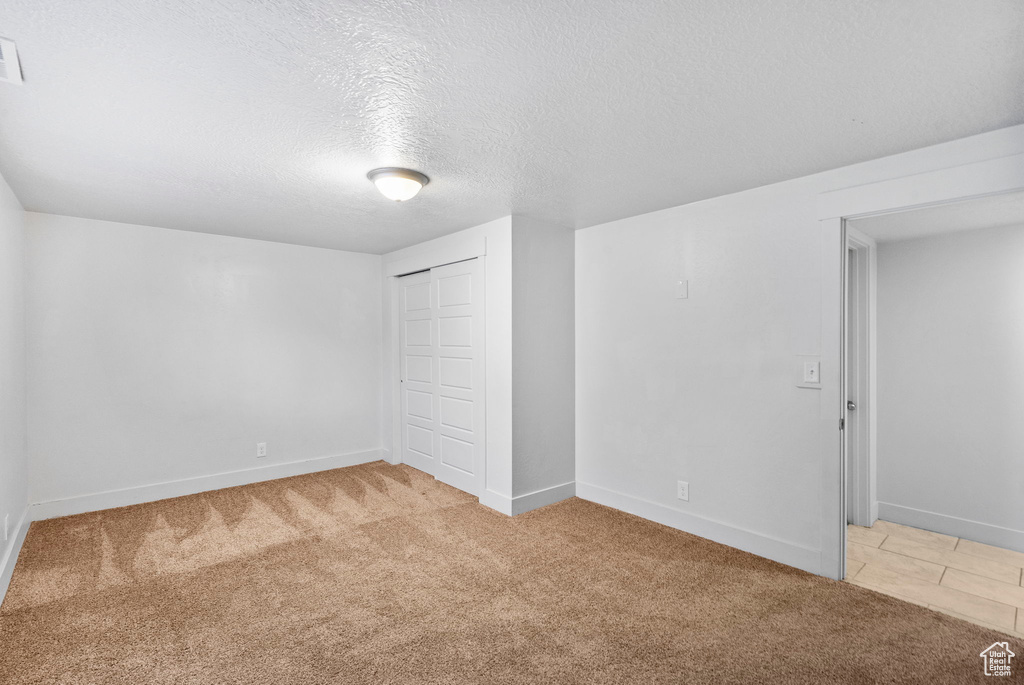 Unfurnished bedroom featuring light colored carpet, a textured ceiling, baseboards, and a closet