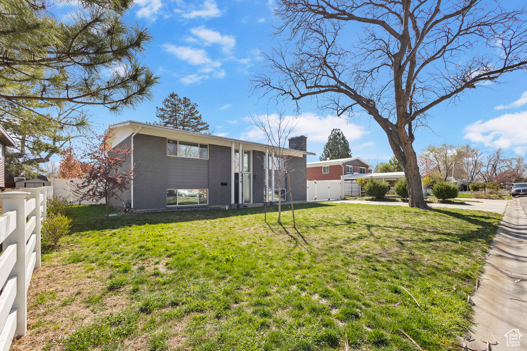 View of front of house with brick siding, a front yard, fence, and a chimney