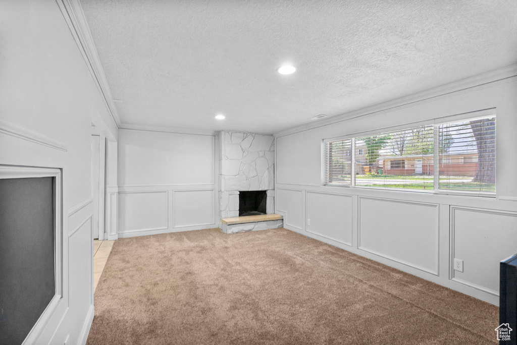 Unfurnished living room featuring a textured ceiling, a fireplace, ornamental molding, carpet, and a decorative wall